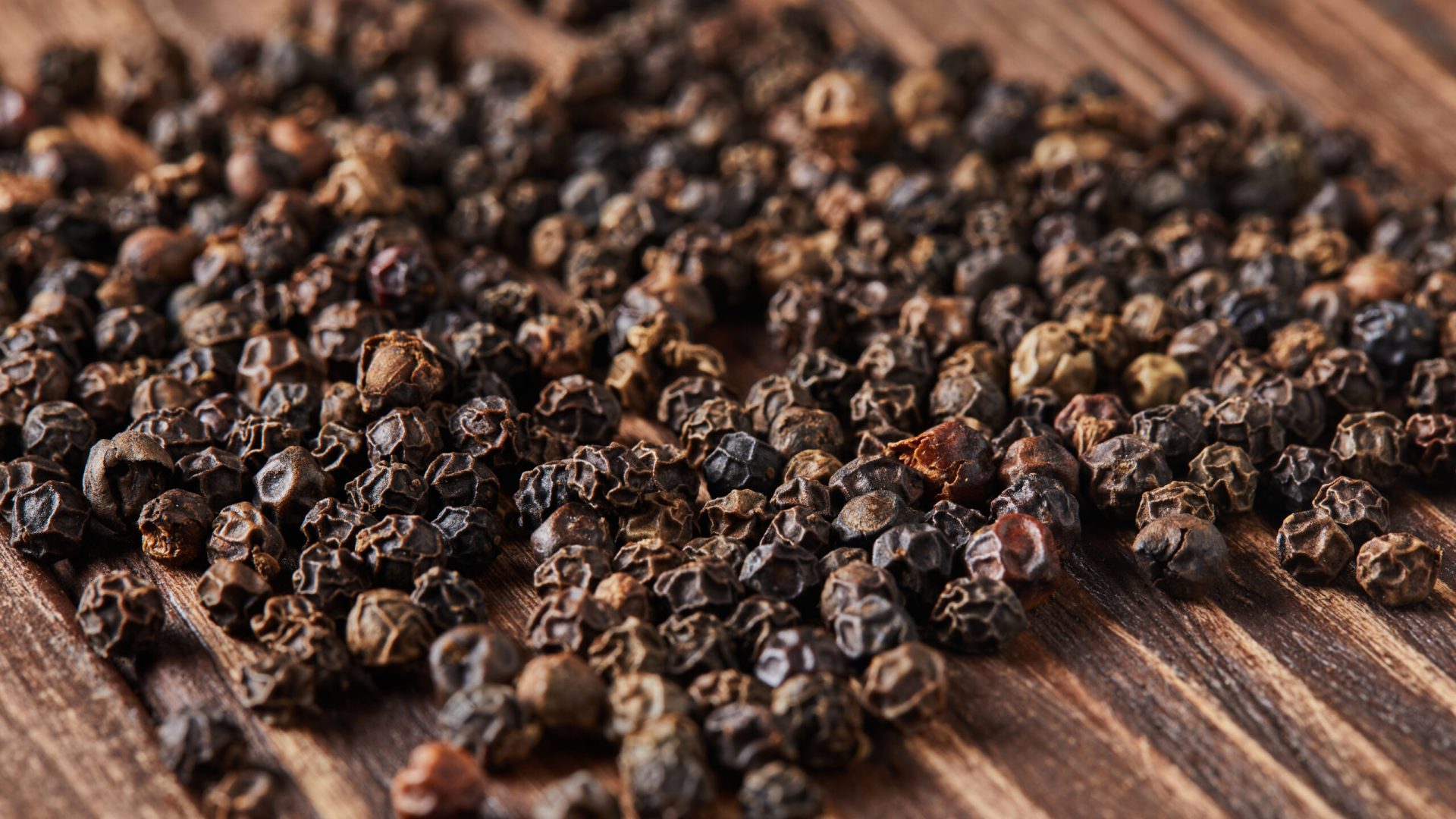 Black peppers are scattered over vintage wood background.