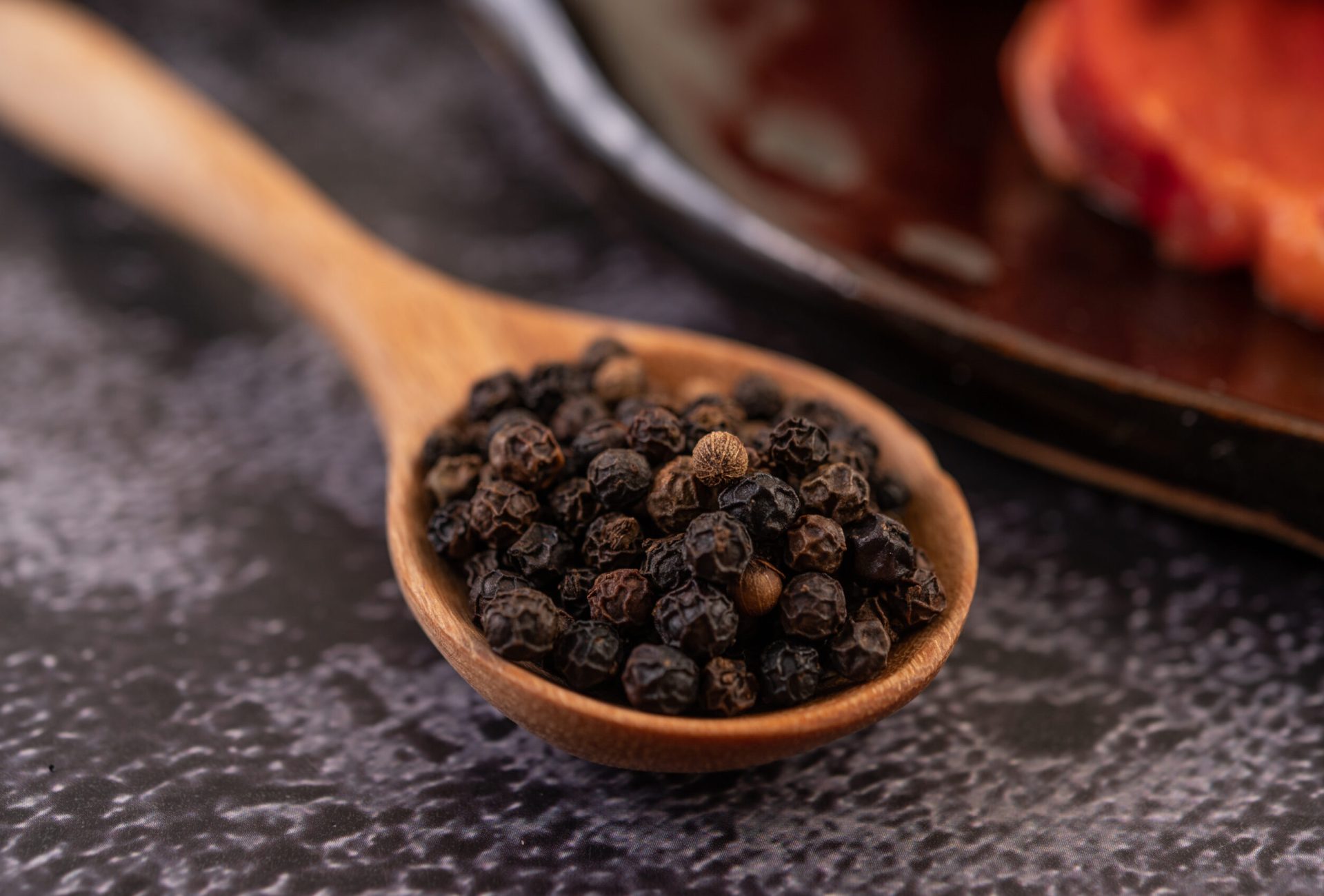 Pepper seeds in a wooden spoon on the black cement floor. Selective focus.